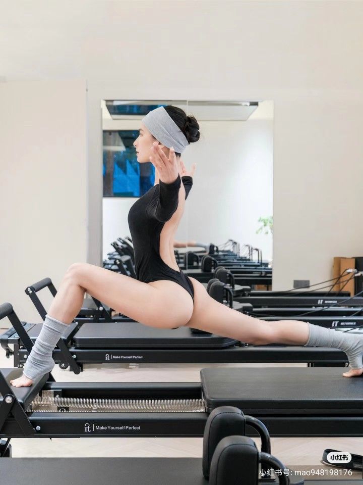 Woman in a black bodysuit doing a split on a pilates reformer