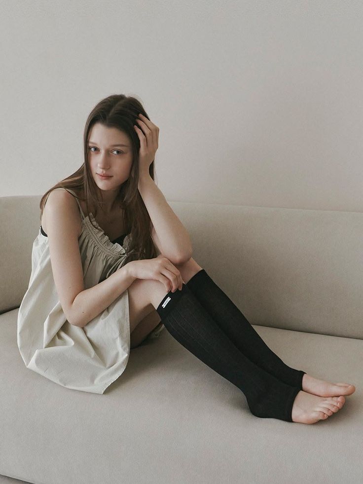 Woman with long hair sitting on a couch in a sleeveless dress and black socks
