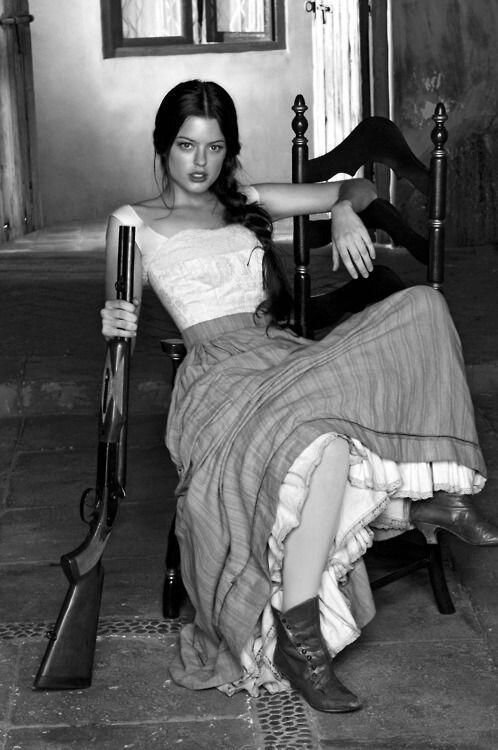 Woman with a shotgun sitting on a chair in a long skirt and boots