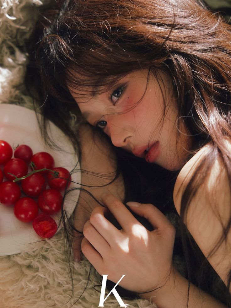 Woman with long hair and red blush lying down with cherry tomatoes