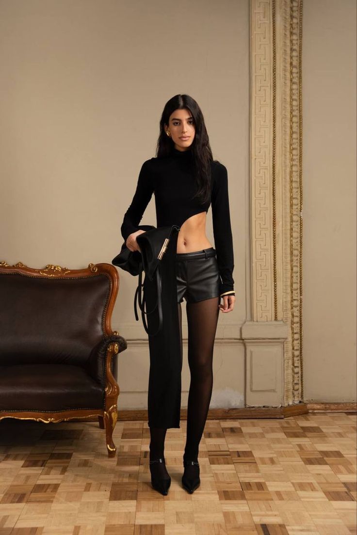 Woman in a black top and leather shorts with exposed midriff in an elegant room