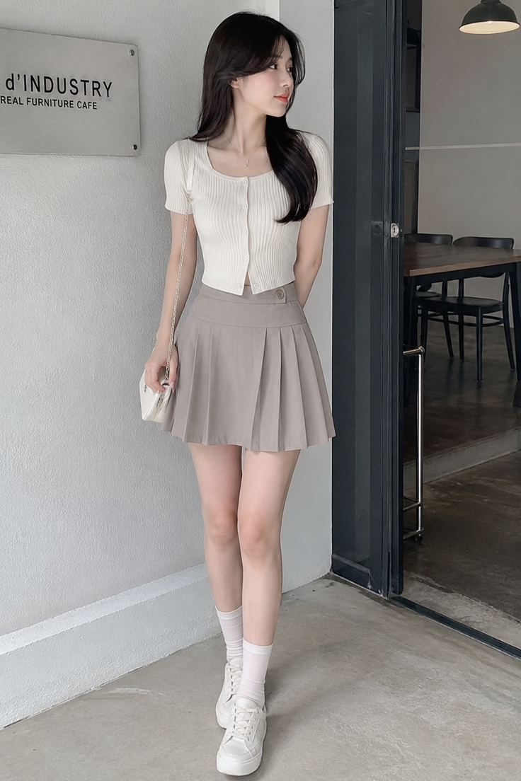 Woman in a white crop top and pleated skirt standing indoors