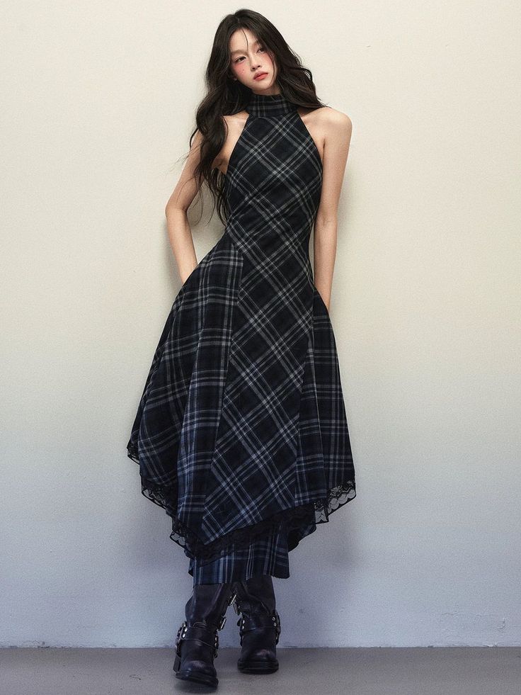 Woman in a plaid halter neck dress and black boots against a plain wall