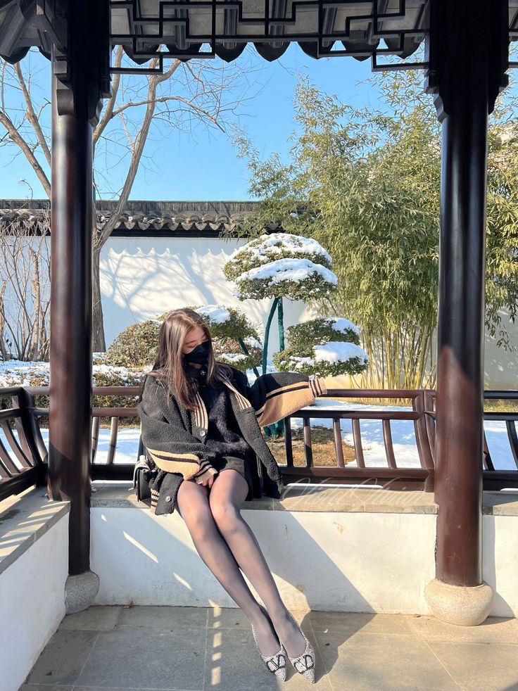 Woman in a black coat and tights sitting outdoors in a snowy garden