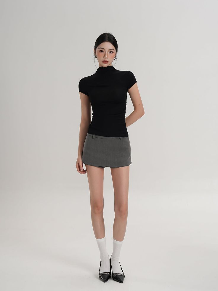 Woman in a black top and grey mini skirt posing in a studio