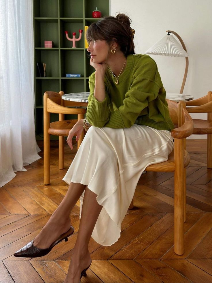 Woman in a green sweater and cream midi skirt sitting indoors