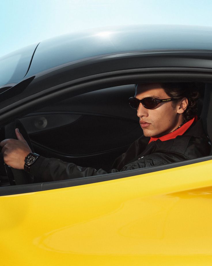 Man in sunglasses and a black jacket driving a yellow car