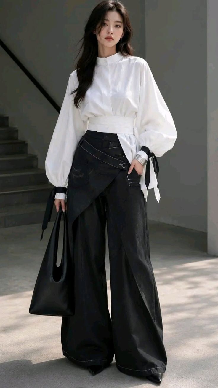 Woman in a white blouse and black wide-leg pants holding a black bag outdoors
