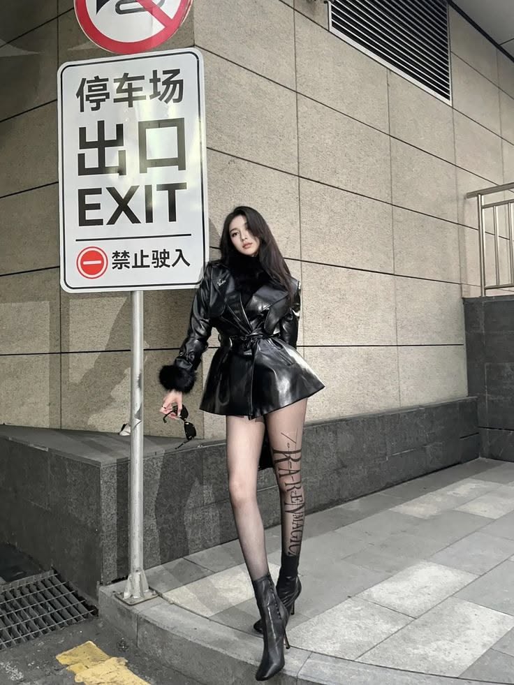 Woman in a black leather jacket and tights standing next to an exit sign