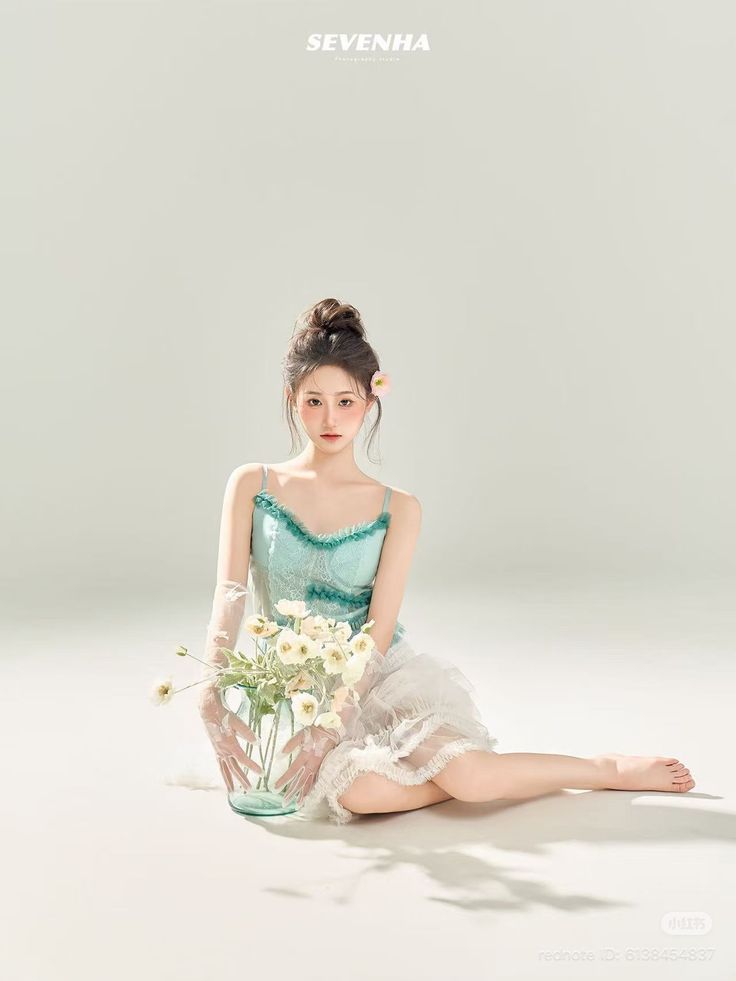 Woman with an updo and flower in her hair, wearing a light blue top and white skirt, holding flowers