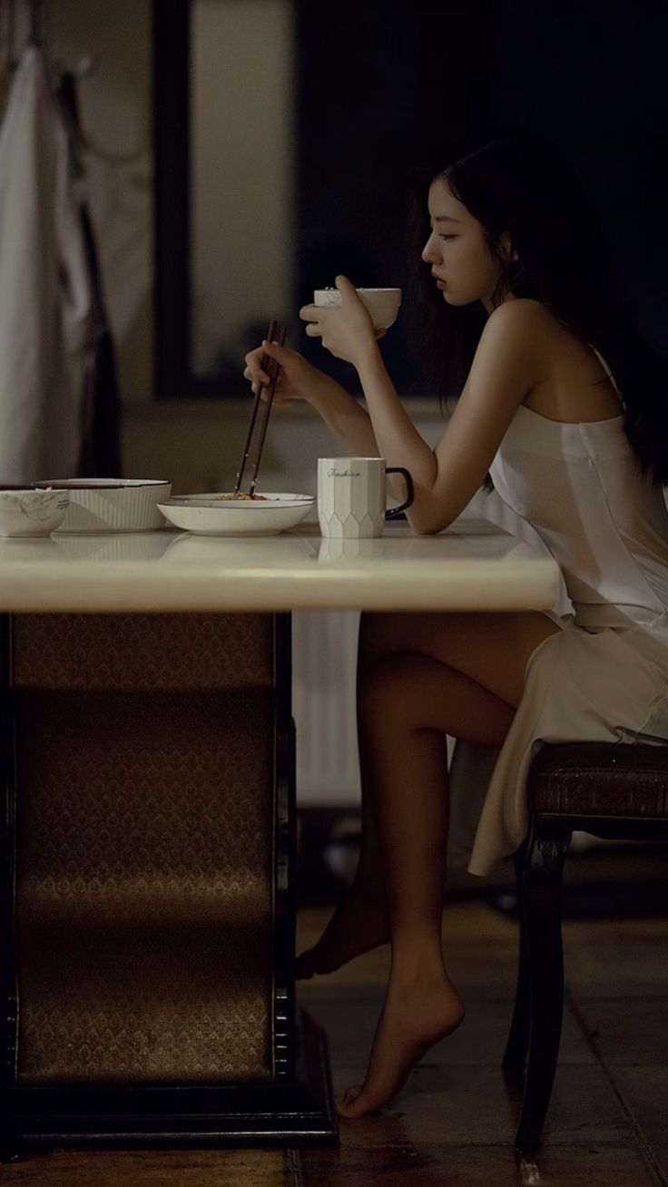 Woman in a white dress eating with chopsticks at a table indoors