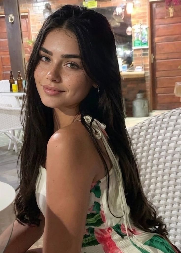 Woman with long dark hair and freckles wearing a floral dress indoors