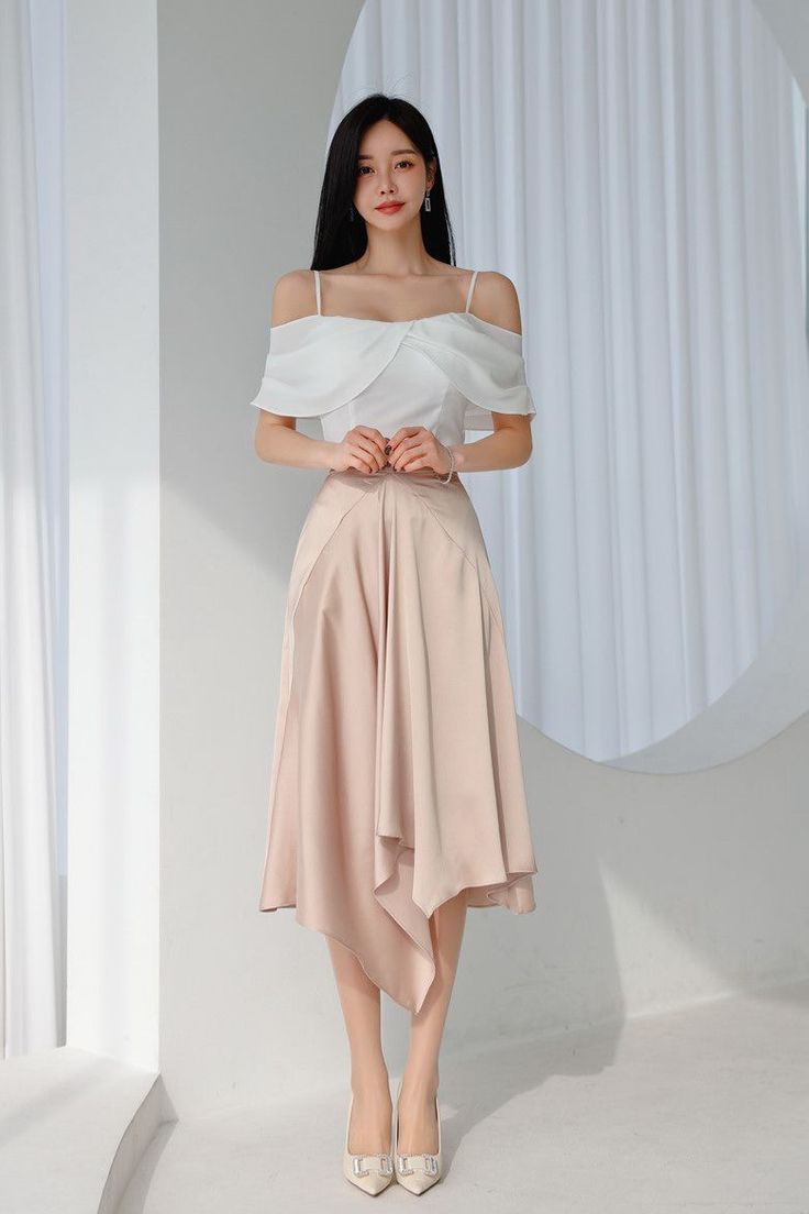 Woman in a white off-shoulder top and a pink asymmetrical skirt standing indoors