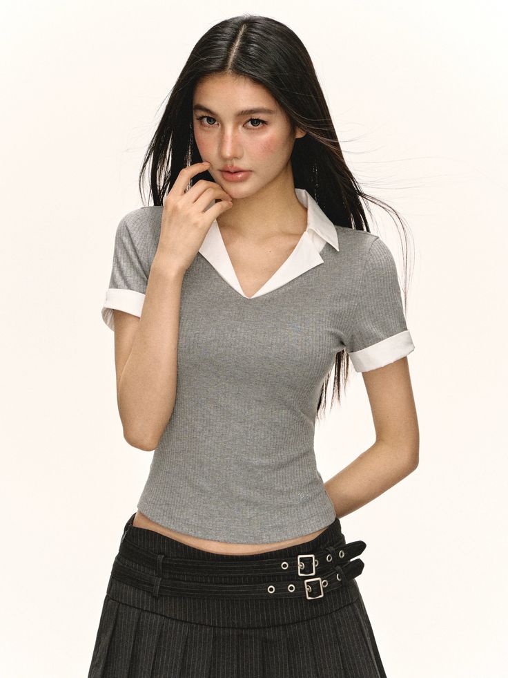 Woman with long dark hair in a grey top and pleated skirt with exposed midriff