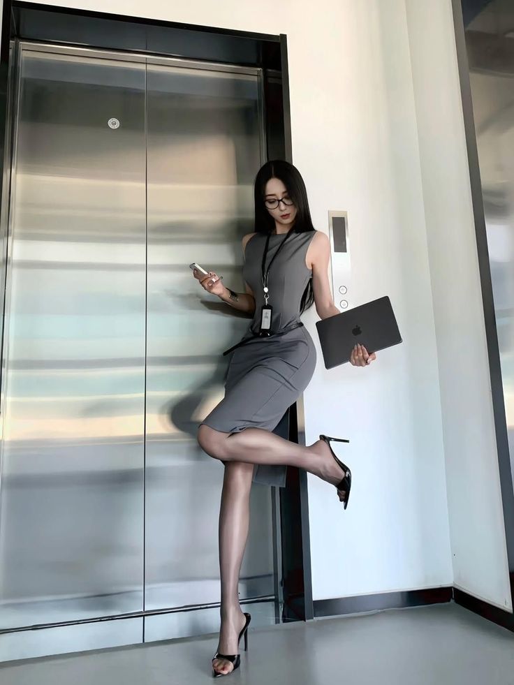 Woman in a gray dress and high heels posing by an elevator