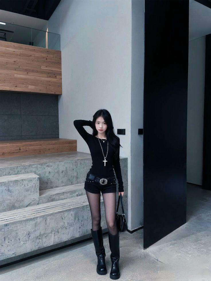 Woman in a black long-sleeve shirt and shorts with black boots indoors