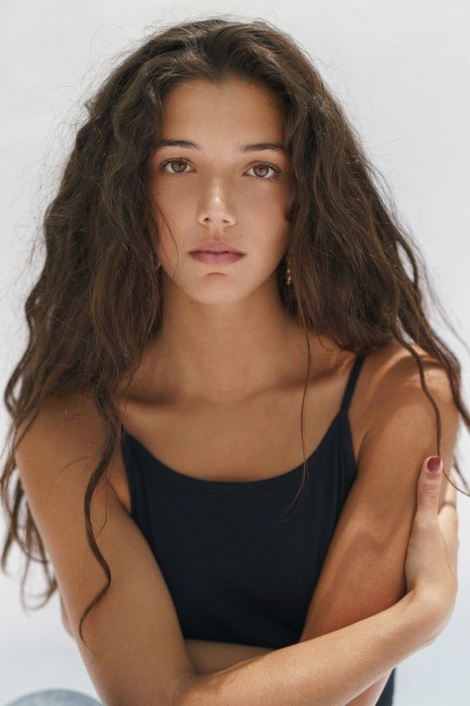 Woman with long wavy hair wearing a black tank top against a white background