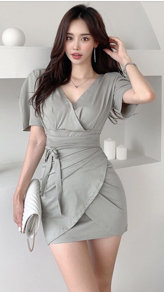 Woman in a light green wrap dress with long dark hair indoors