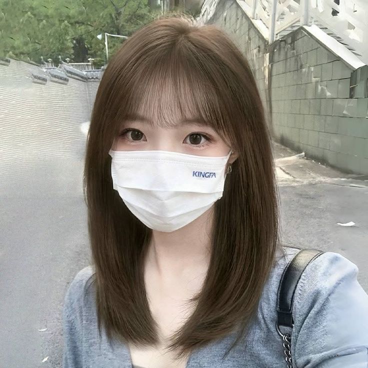 Woman with brown hair and bangs wearing a white mask and gray cardigan outdoors