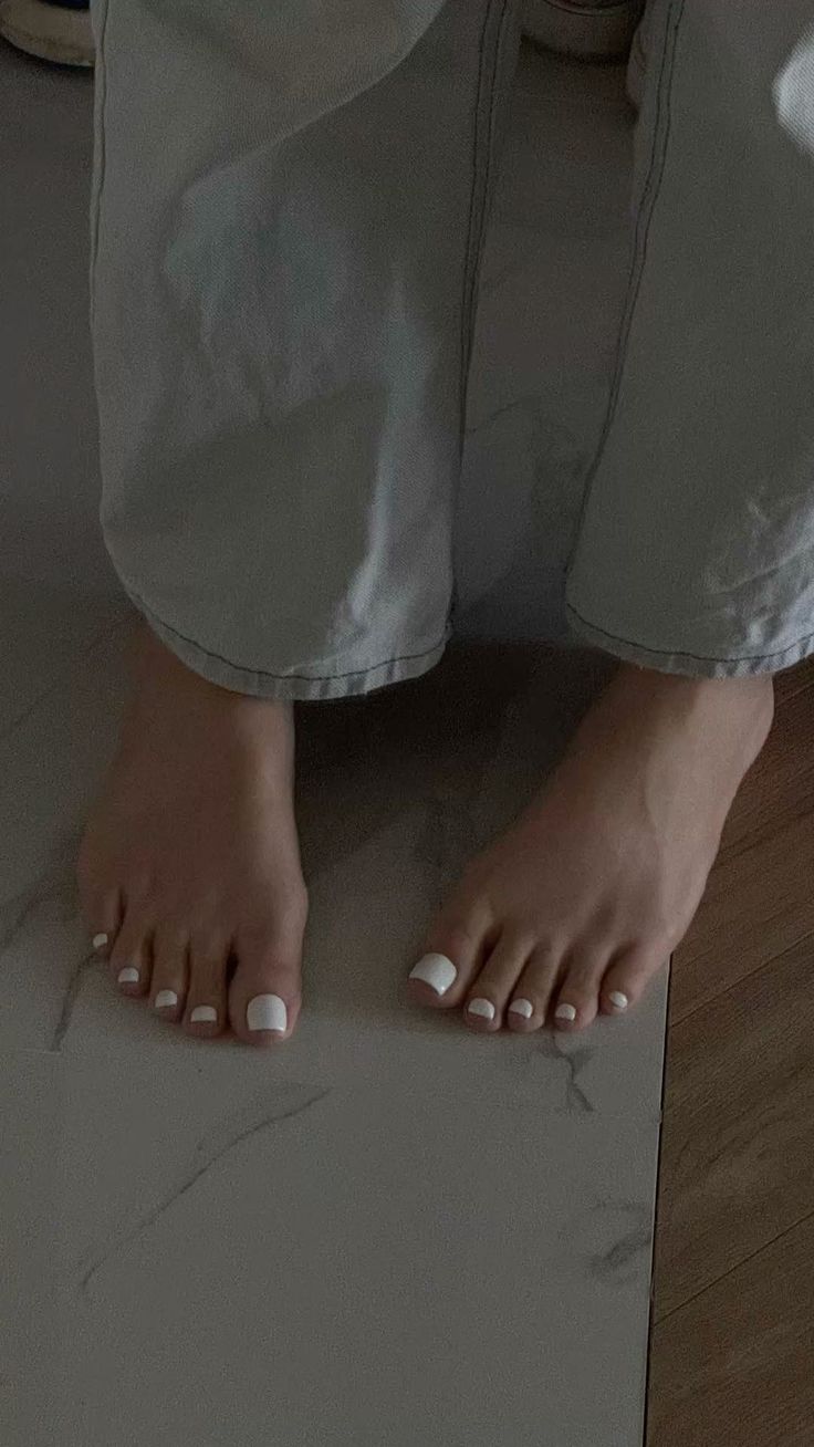 Person's bare feet with white toenails on a tiled floor, wearing light wash jeans