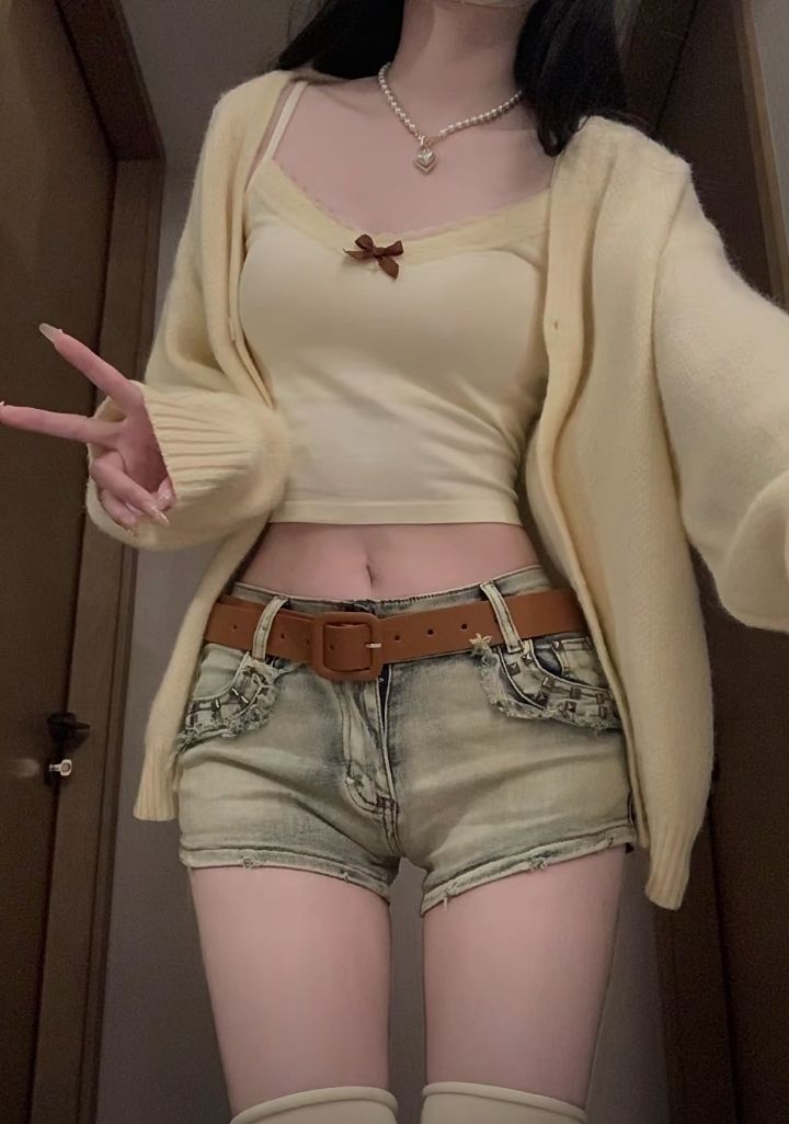 Person in a crop top, cardigan, and denim shorts showing peace sign