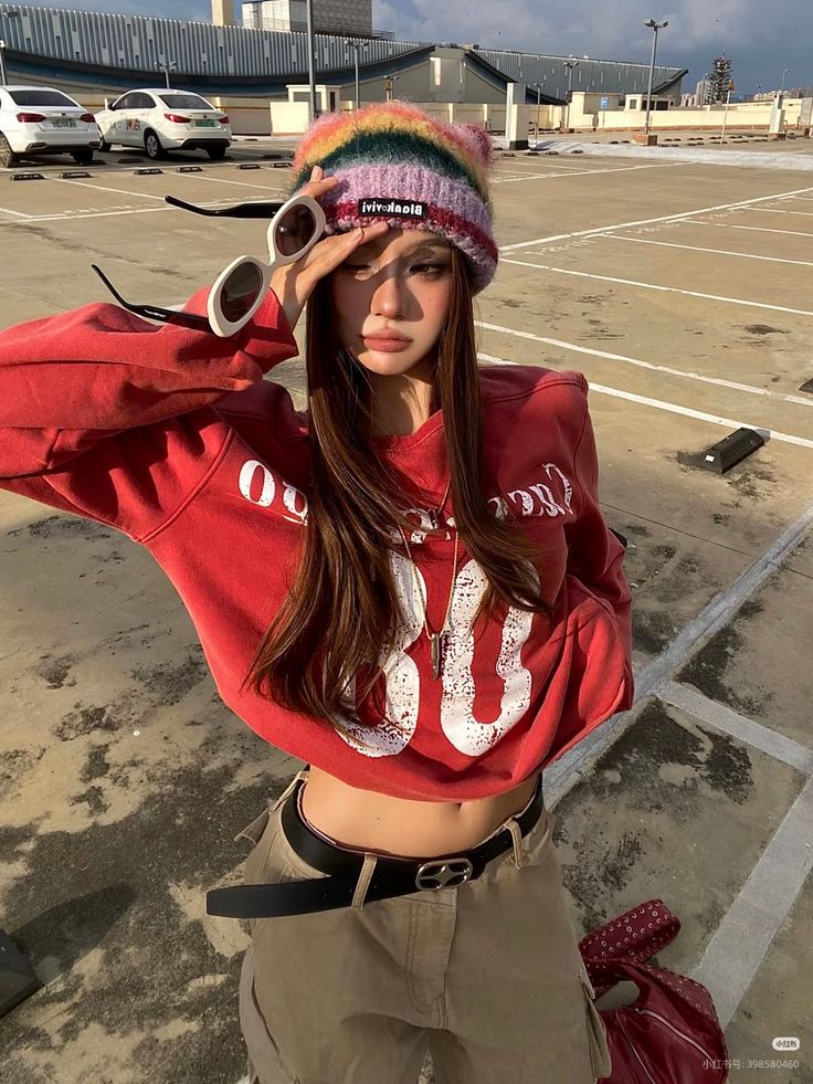 Woman in a rainbow beanie and cropped sweatshirt posing in a parking lot