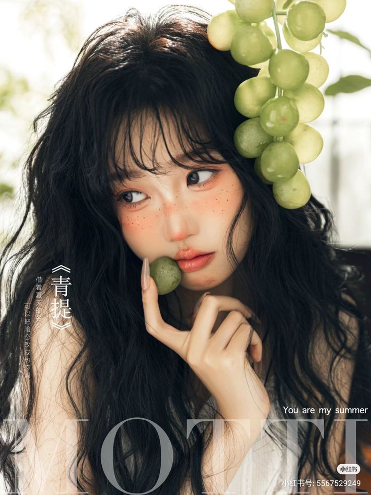 Woman with long dark hair and freckles holding a green grape