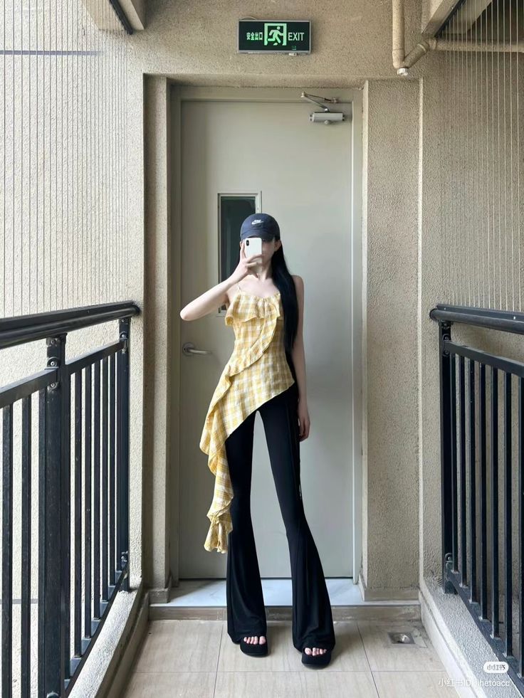 Woman in a plaid ruffle top and flared pants taking a mirror selfie indoors
