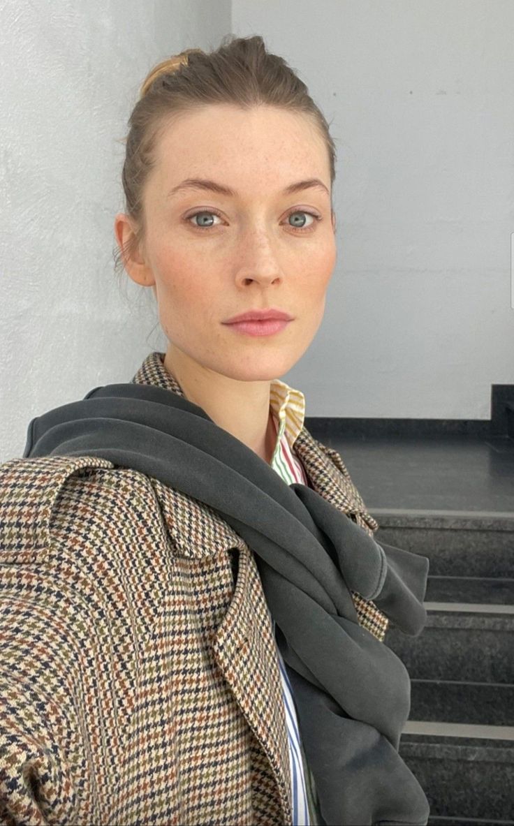 Woman with a hair bun and freckles wearing a houndstooth jacket indoors