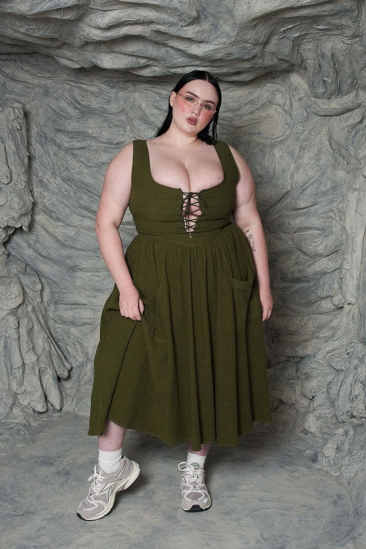 Woman in an olive green dress with a laced bodice and sneakers in a studio