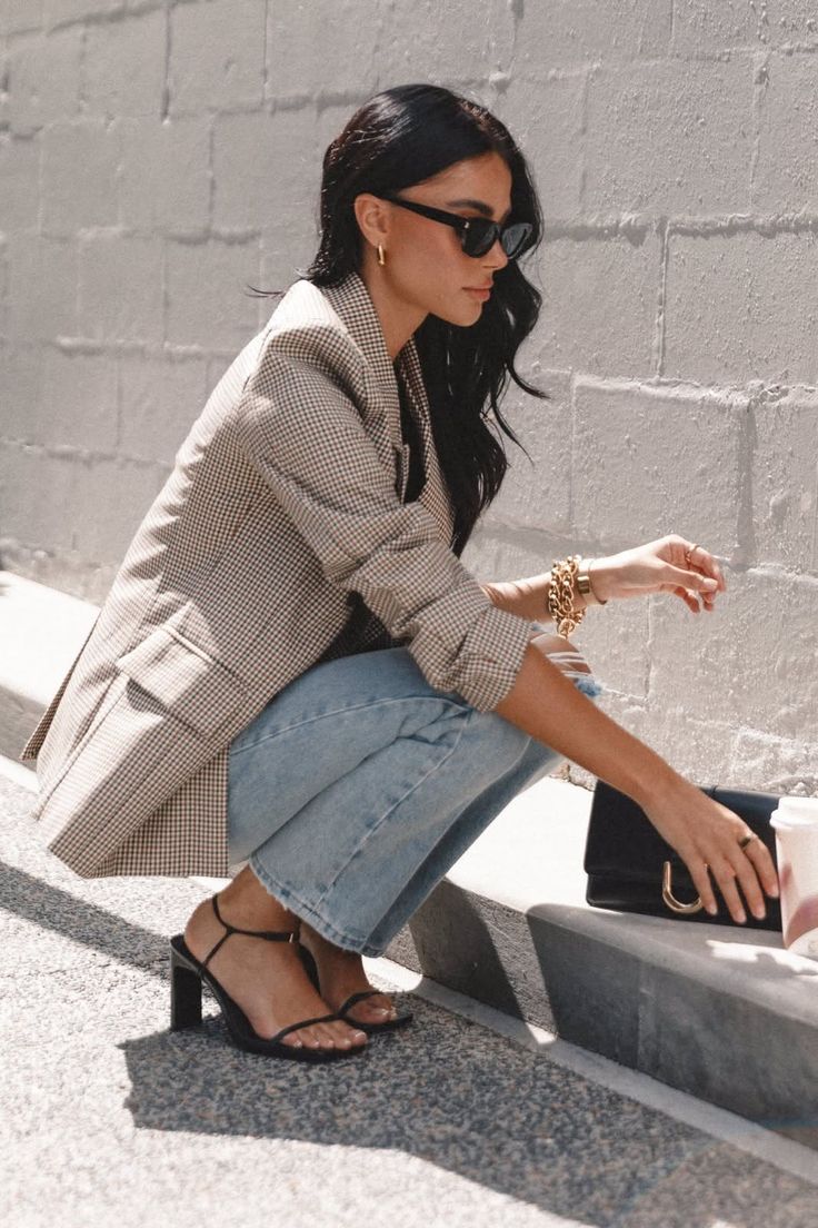 Woman in a plaid blazer and jeans crouching outdoors