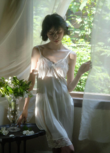 Woman in white lace lingerie standing by a window with soft lighting