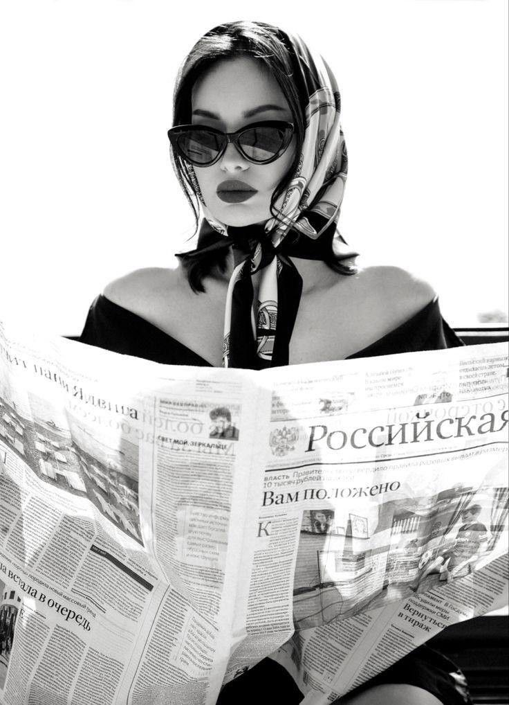 Woman in a head scarf and sunglasses reading a newspaper in black and white