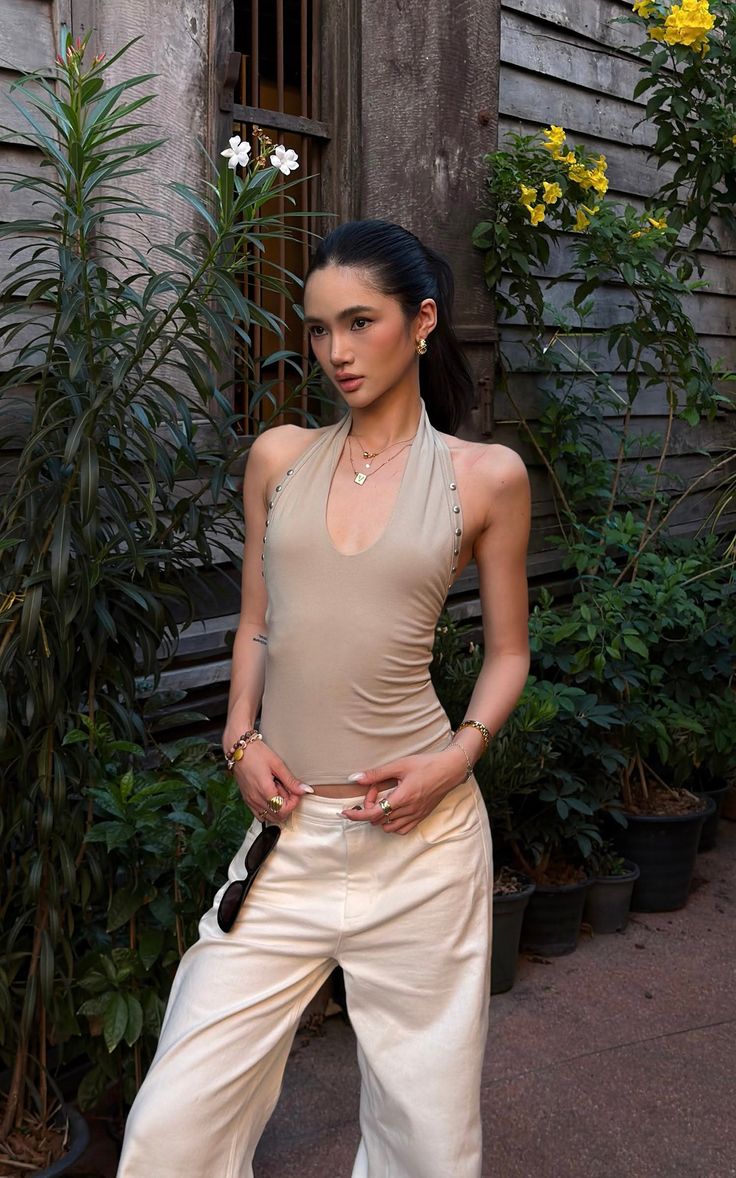 Woman in a beige halter top and light pants posing outdoors