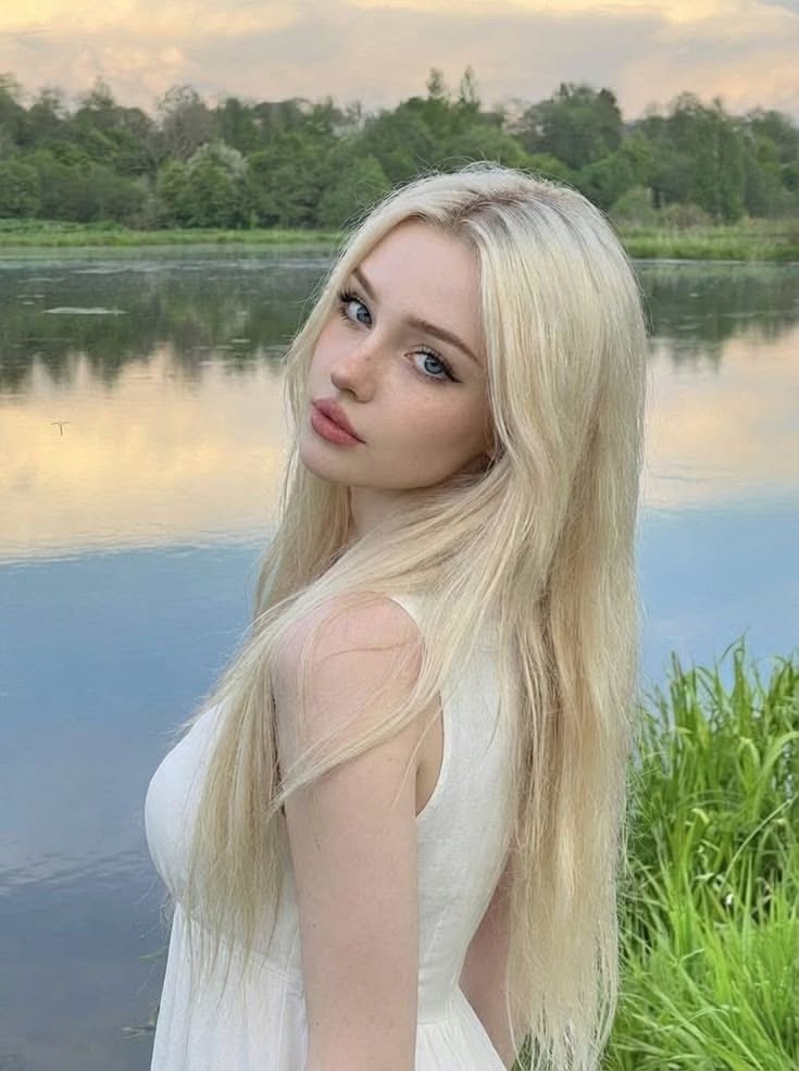 Blonde woman in a white dress by a lake with soft lighting