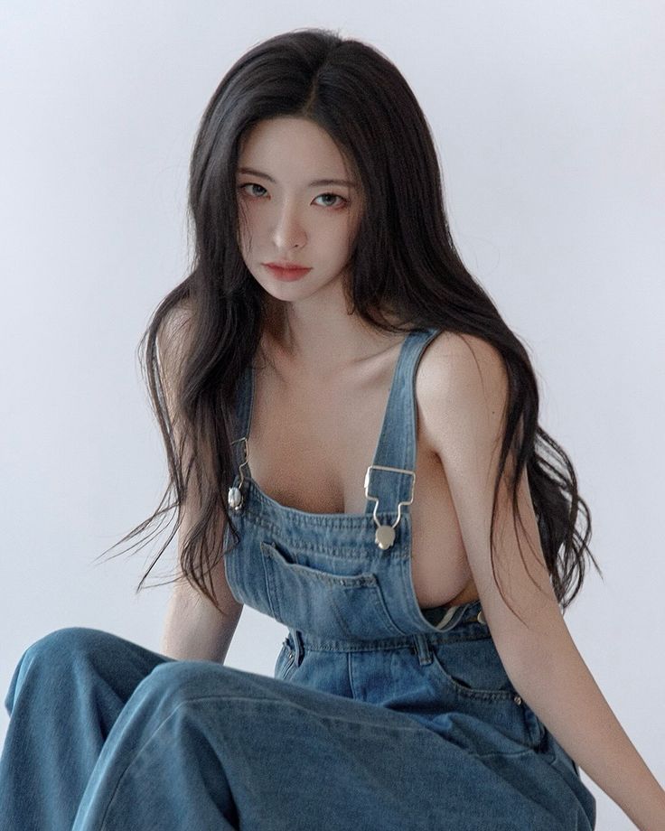 Woman with long black hair wearing denim overalls in a studio setting
