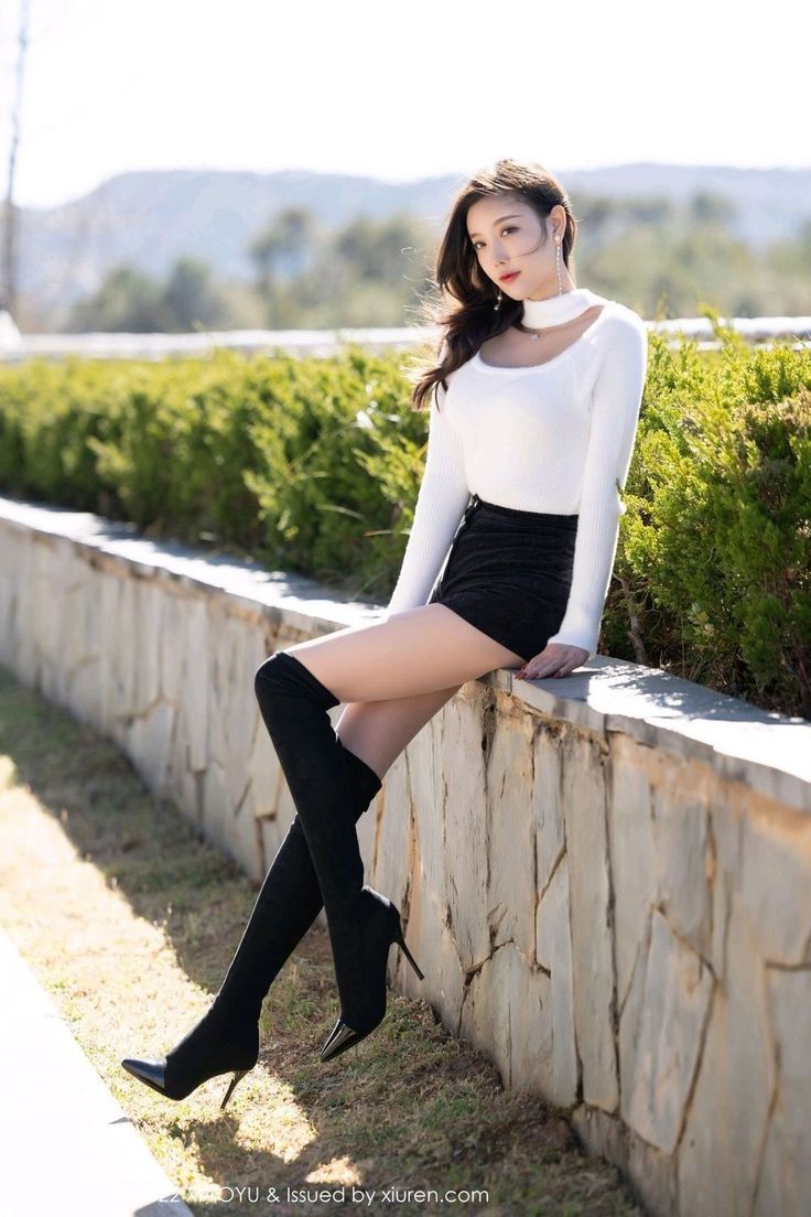 Woman in a white sweater and black shorts with thigh-high boots outdoors