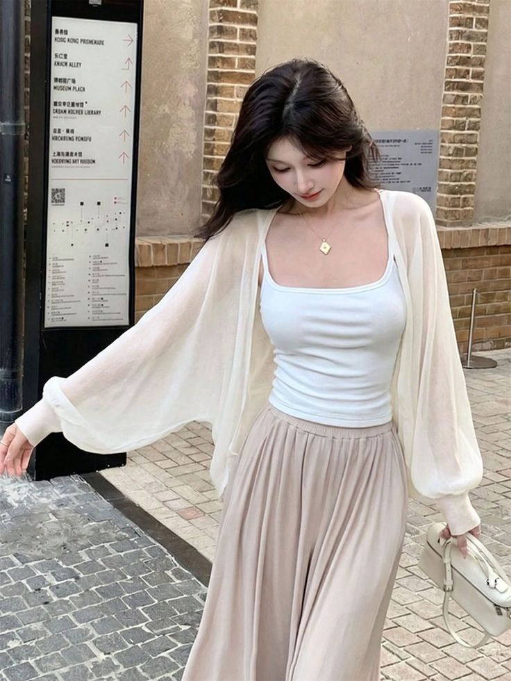 Woman with long dark hair wearing a white tank top and sheer cardigan outdoors