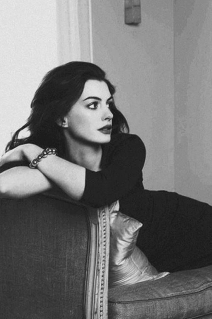 Woman with dark hair and a bracelet, leaning on a couch in a black and white portrait