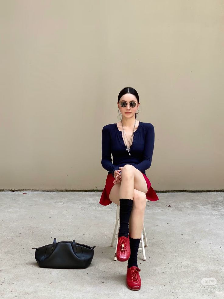 Woman with long hair and sunglasses sitting outdoors in a red skirt