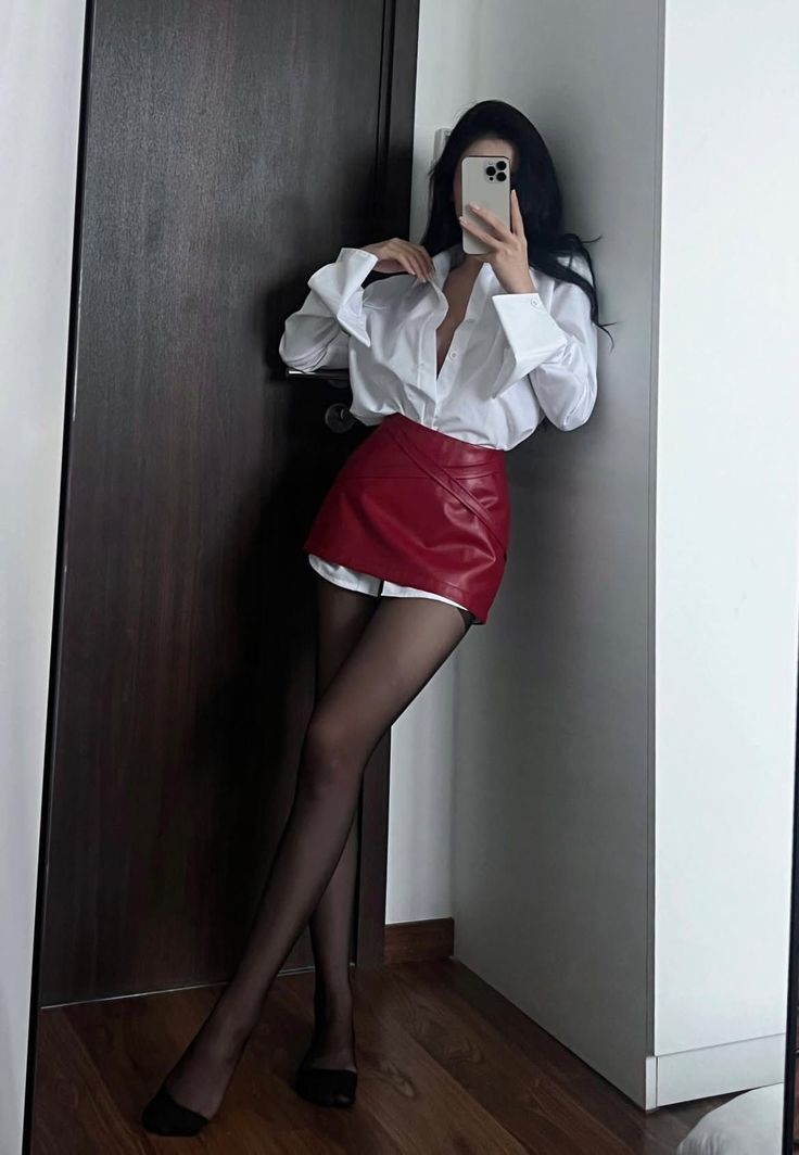 Woman in a red mini skirt and white shirt taking a mirror selfie