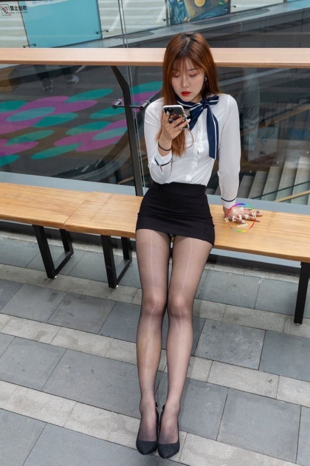 Woman in a white shirt and black mini skirt sitting on a bench outdoors