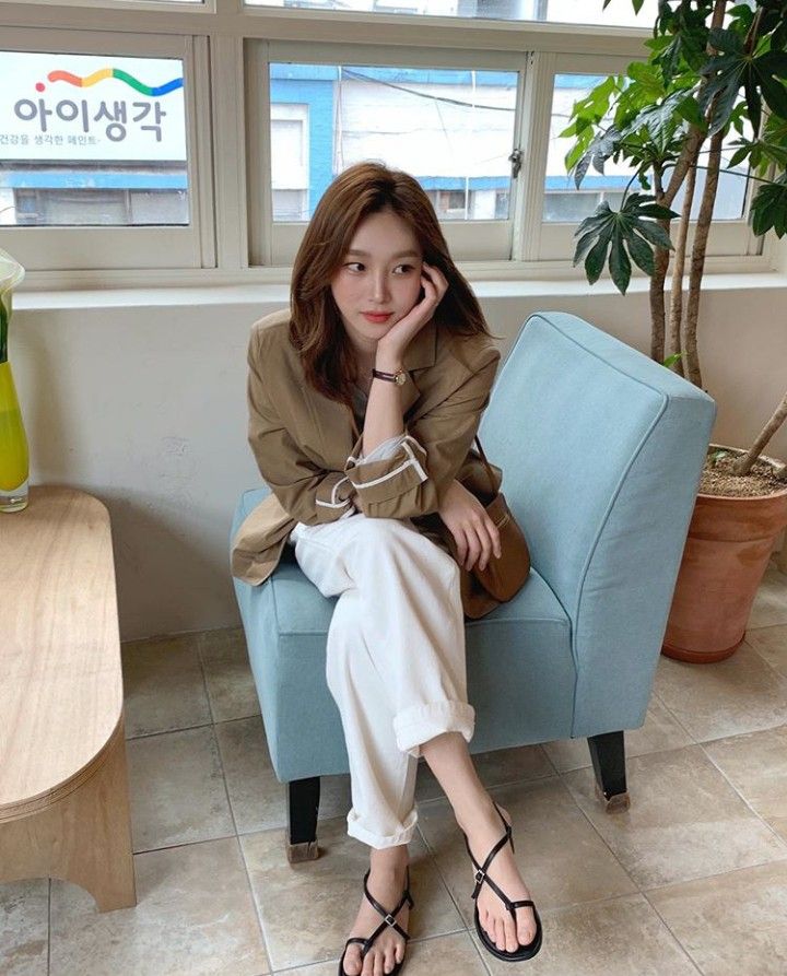 Woman with brown hair wearing a brown blazer and white pants, sitting indoors