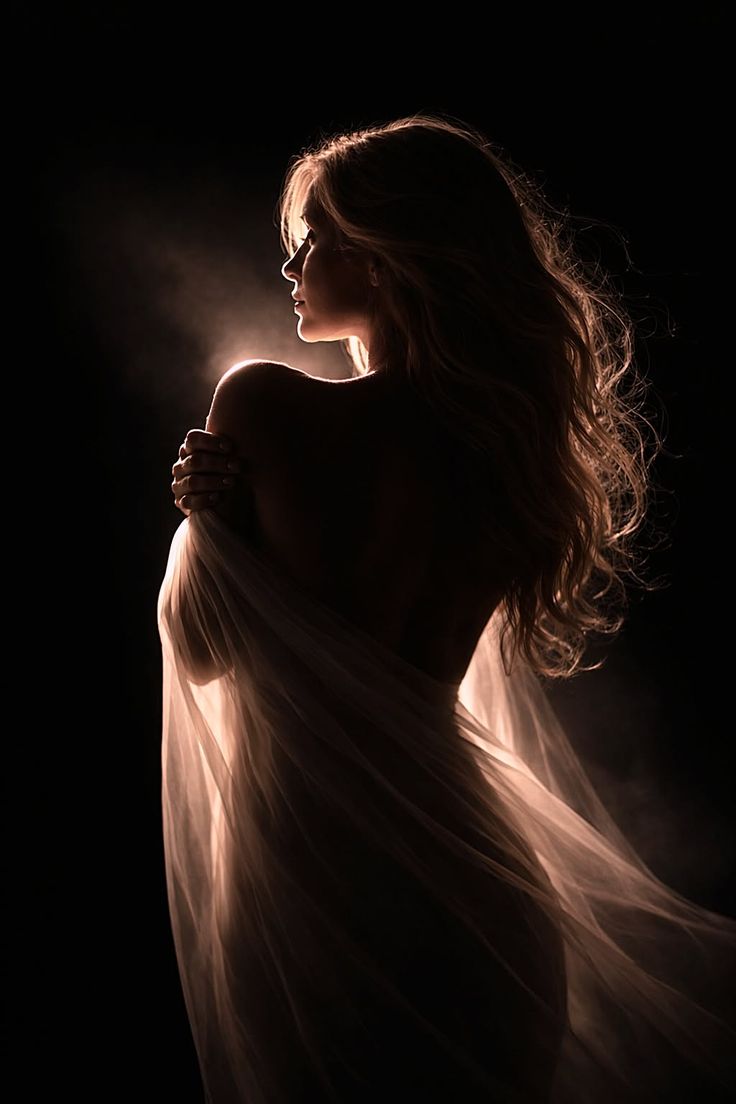 Woman with long hair in dramatic backlight, draped in sheer fabric
