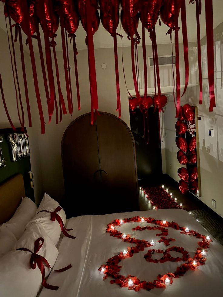 Bedroom decorated with red heart balloons, rose petals, and candles for a romantic occasion