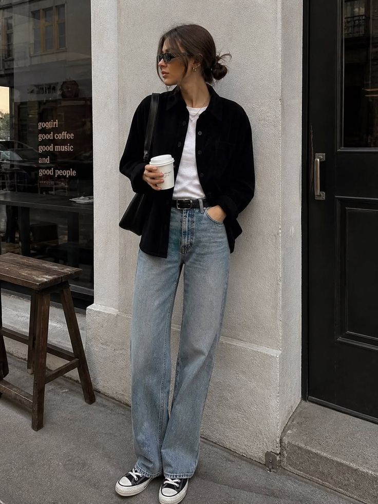 Woman in loose jeans and a black shirt holding a coffee cup on a street