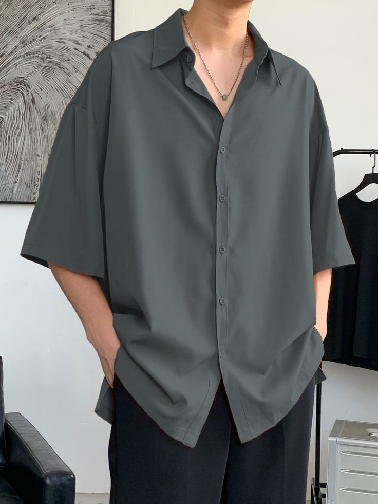 Person wearing a dark grey oversized short-sleeve shirt and black pants indoors