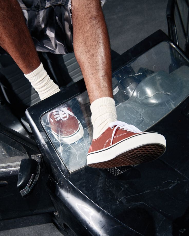 Person wearing red sneakers and white socks with camo shorts on a car window