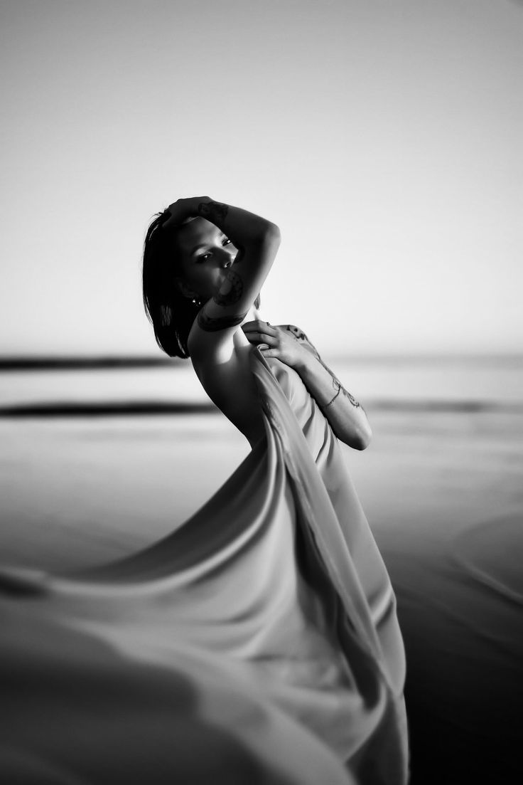 Woman with short hair and tattoos posing on a beach with flowing fabric