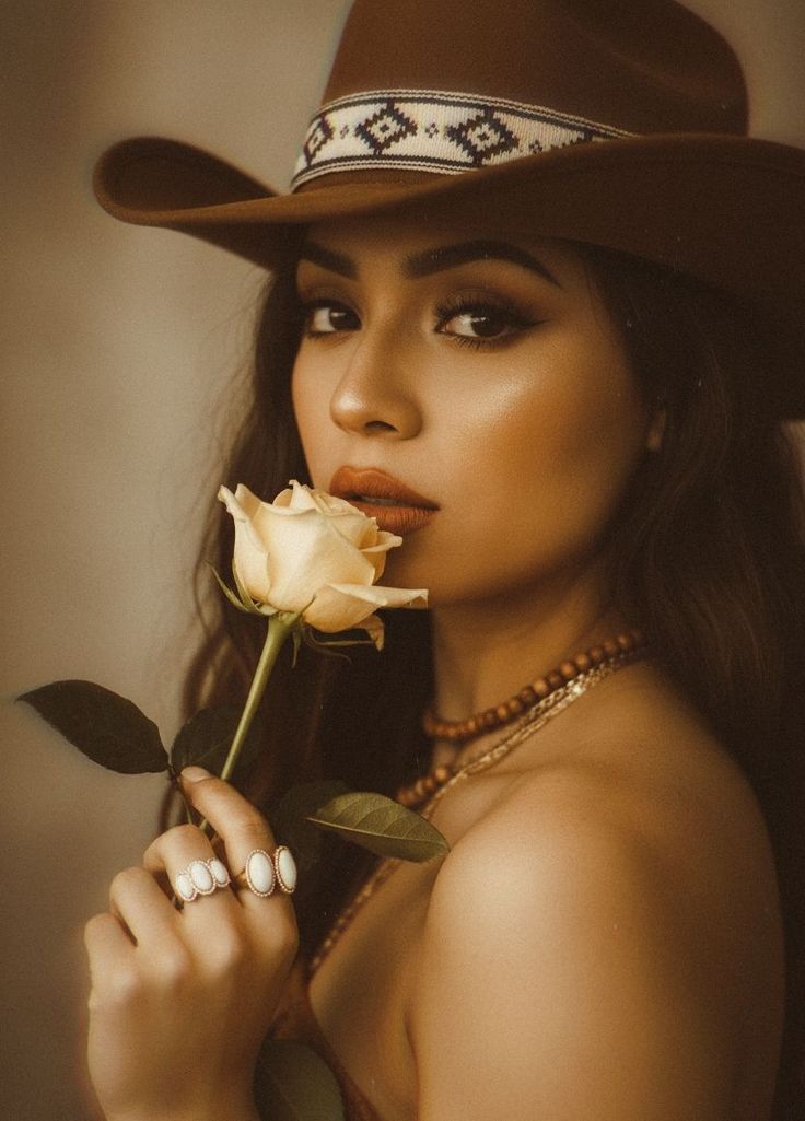 Woman in a cowboy hat holding a yellow rose to her lips